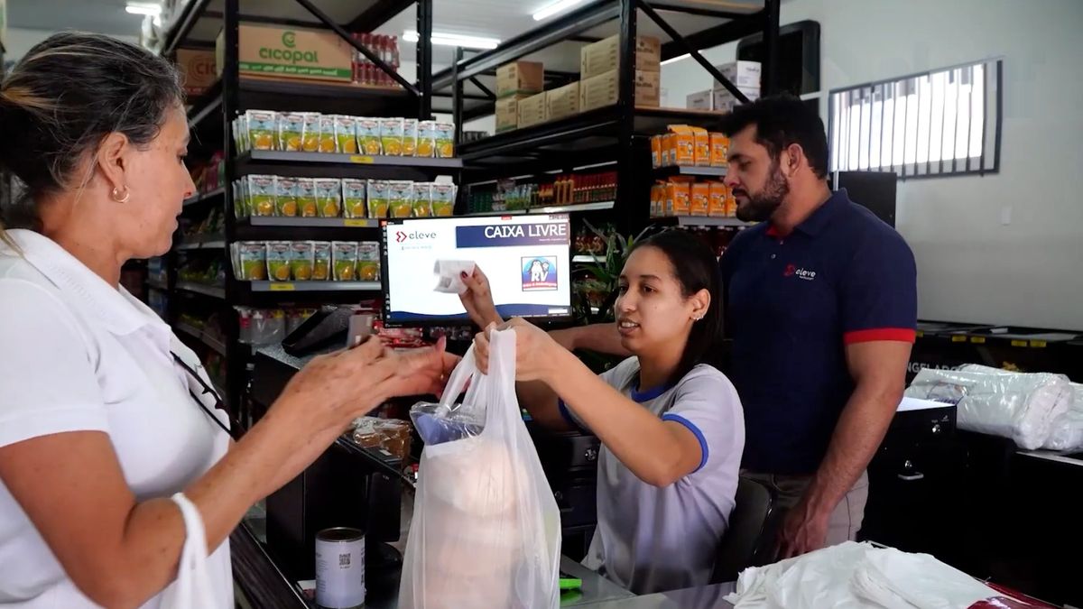 Operadora de caixa sorrindo em frente ao PDV de um supermercado